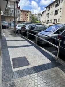 Acceso peatonal con barandilla en una calle con vehículos estacionados