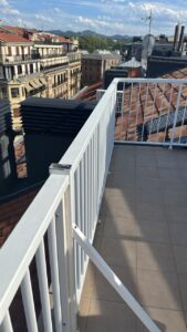 Barandilla blanca de terraza con vista a edificios y montañas al fondo
