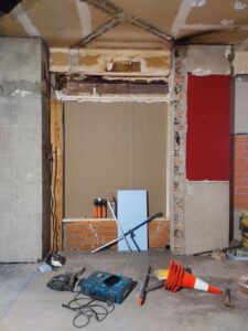 Espacio en proceso de reforma con herramientas y materiales de construcción. Se ven maderas, paneles y una herramienta eléctrica.