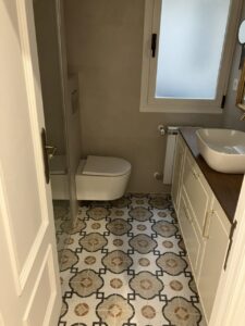 Baño reformado con sanitarios modernos y azulejos decorativos en el suelo