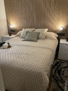 Cama con ropa de cama beige y almohadas decorativas en un dormitorio con cabecero de madera y luces integradas