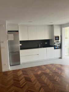 Cocina con muebles blancos y encimera negra, electrodomésticos de acero y suelo de madera clara