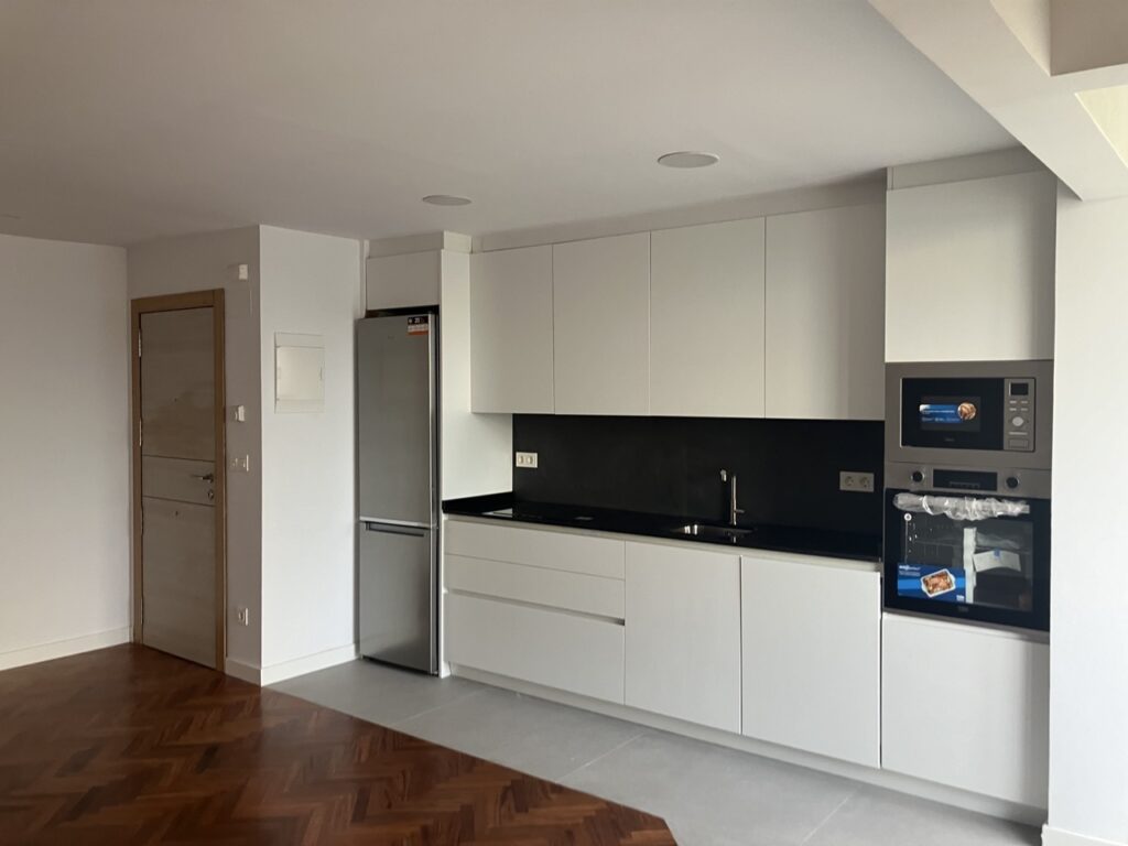 Cocina con mobiliario blanco, encimera negra y electrodomésticos de acero inoxidable