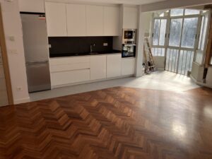 Cocina con muebles blancos y suelo de madera en patrón de espiga