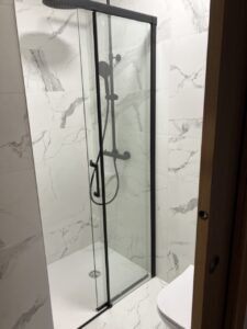 Ducha con mampara de cristal en un baño con azulejos de mármol