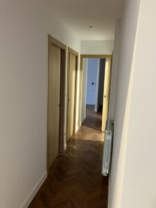 Pasillo con paredes blancas, suelo de madera y puertas de madera