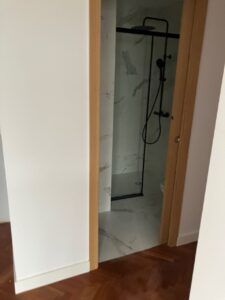 Ducha moderna con acabados en mármol y mampara de vidrio en un baño