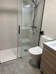 Baño reformado con mampara de ducha y lavabo sobre mueble de madera