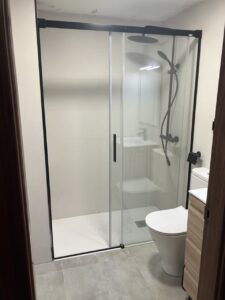 Ducha con mampara de cristal y sanitarios en un baño reformado