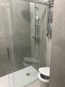 Ducha con mampara de vidrio en un baño, incluye grifería y azulejos en tonos grises