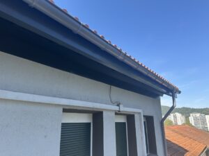 Fachada de vivienda con canalón y tejas en color rojo, cielo despejado al fondo