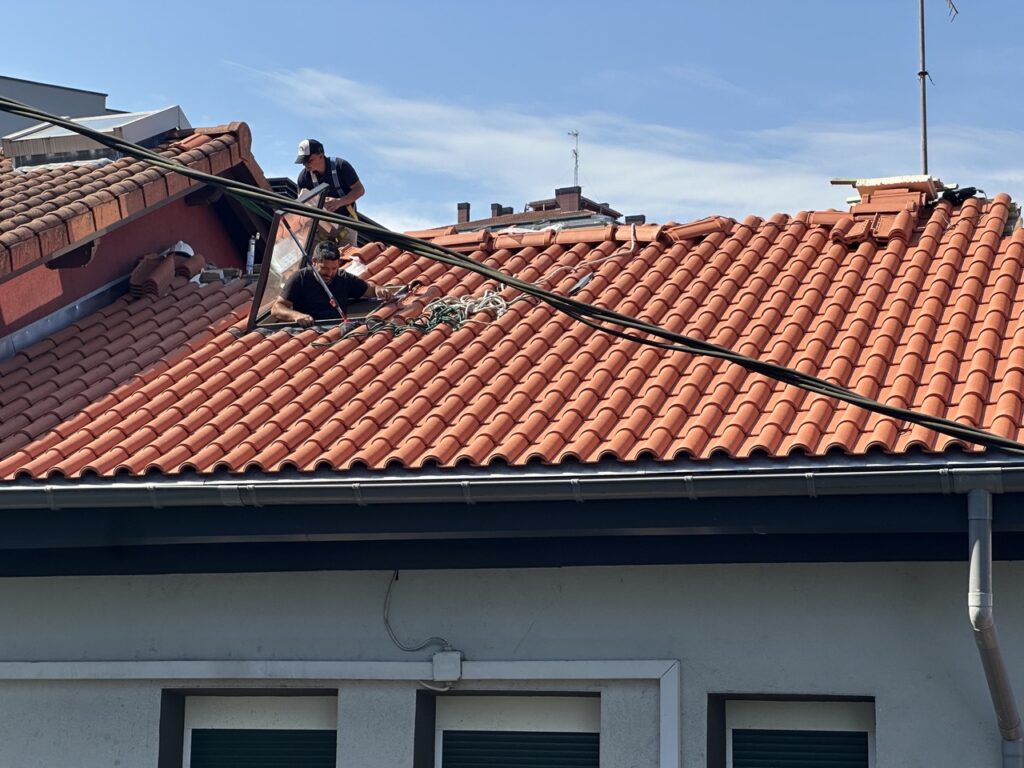 Trabajadores reparando un tejado de tejas rojas sobre una casa