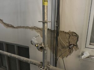 Estructura metálica de andamio junto a una pared dañada con cimentación expuesta
