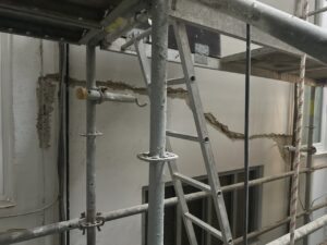 Andamiaje con escalera frente a pared con grietas durante proceso de rehabilitación