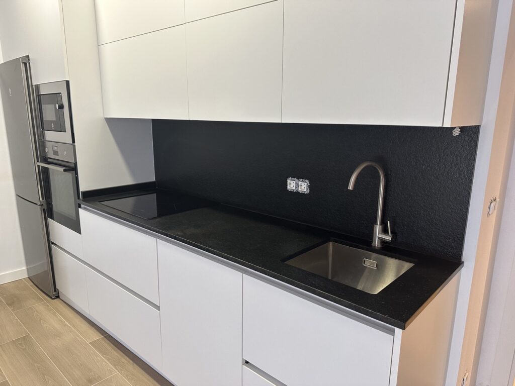 Cocina con muebles blancos y paredes negras, equipada con fregadero y encimera de granito negro.
