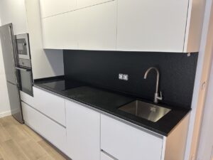 Cocina con muebles blancos y paredes negras, equipada con fregadero y encimera de granito negro.