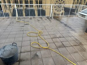 Terraza con baldosas y una manguera amarilla en el suelo junto a un cubo