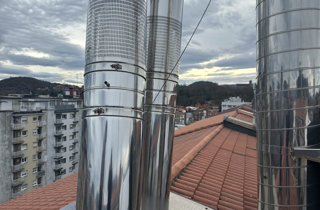 Chimeneas de acero inoxidable en un tejado con vistas a la ciudad y montañas al fondo