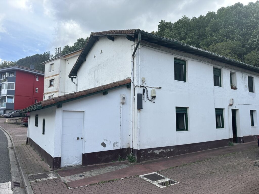 Fachada blanca de una vivienda rehabilitada con ventanas en el lateral.