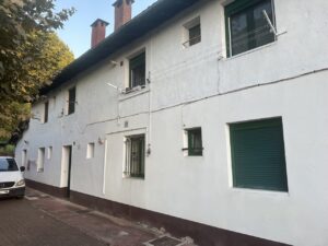 Fachada blanca de edificio con ventanas verdes y una puerta en la calle