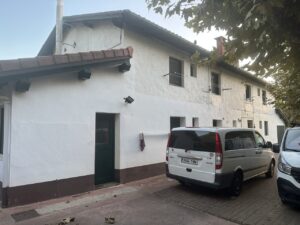 Fachada de vivienda con color blanco, puertas y ventanas oscuros, y vehículo estacionado