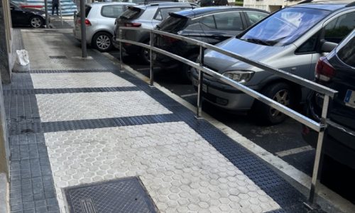 Acceso peatonal con barandilla en una calle con vehículos estacionados
