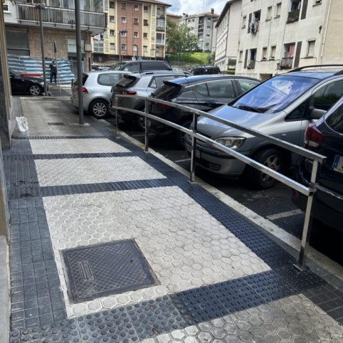 Acceso peatonal con barandilla en una calle con vehículos estacionados