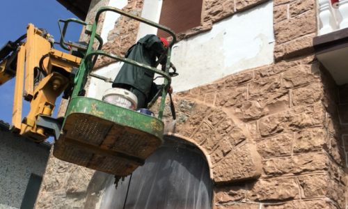 Trabajador en canasta elevadora realizando reformas en una fachada de piedra color beige