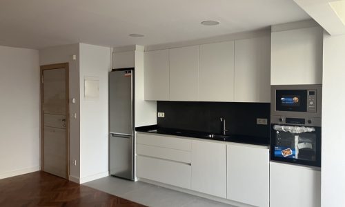 Cocina con mobiliario blanco, encimera negra y electrodomésticos de acero inoxidable