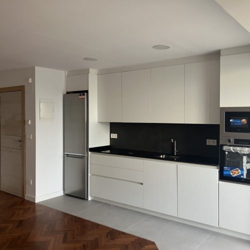 Cocina con mobiliario blanco, encimera negra y electrodomésticos de acero inoxidable