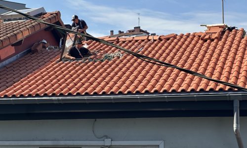 Trabajadores reparando un tejado de tejas rojas sobre una casa