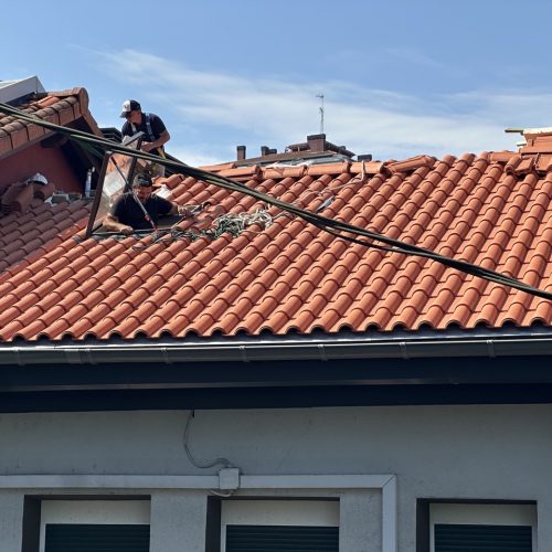 Trabajadores reparando un tejado de tejas rojas sobre una casa