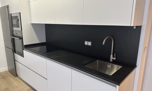Cocina con muebles blancos y paredes negras, equipada con fregadero y encimera de granito negro.