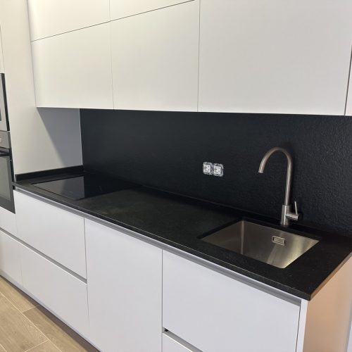 Cocina con muebles blancos y paredes negras, equipada con fregadero y encimera de granito negro.