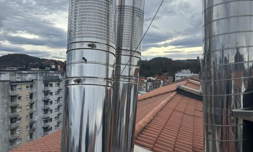 Chimeneas de acero inoxidable en un tejado con vistas a la ciudad y montañas al fondo
