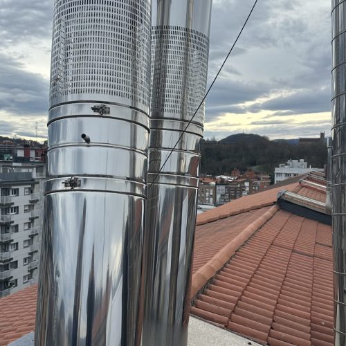 Chimeneas de acero inoxidable en un tejado con vistas a la ciudad y montañas al fondo