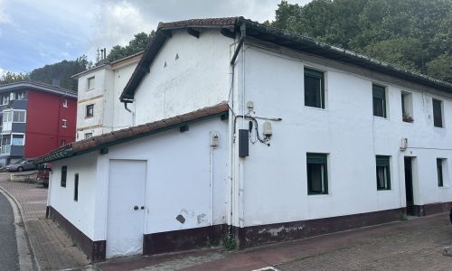Fachada blanca de una vivienda rehabilitada con ventanas en el lateral.
