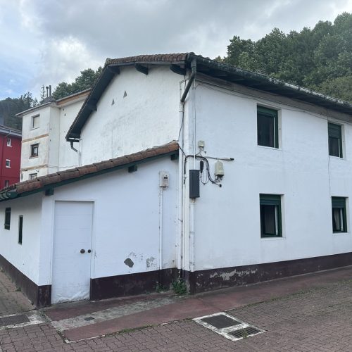 Fachada blanca de una vivienda rehabilitada con ventanas en el lateral.